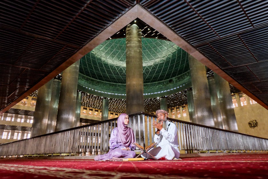 Foto estetik seorang anak muda Muslim sedang duduk santai di sebuah kafe modern dengan pencahayaan hangat, ia sedang memegang buku catatan atau jurnal, di meja ada secangkir kopi, dan ia tampak tersenyum tenang sambil melihat ke arah jendela.