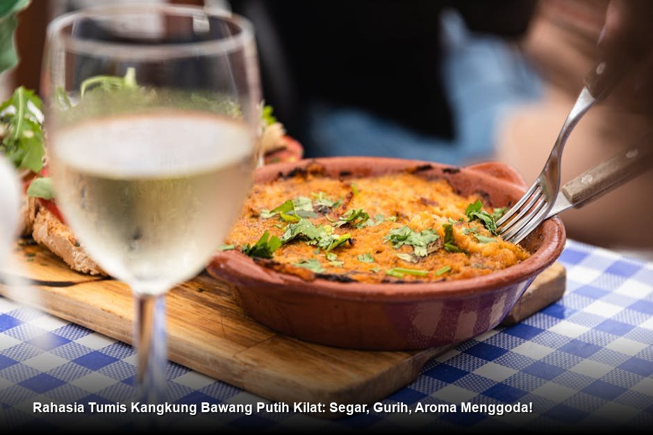 Tumis kangkung bawang putih yang baru matang, disajikan di piring putih dengan taburan bawang putih goreng renyah yang mengkilap.
