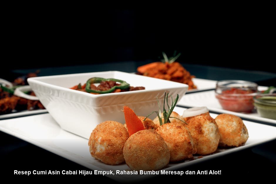 Sepiring Cumi Asin Cabai Hijau yang mengkilap dengan minyak bumbu, dihiasi irisan tomat hijau segar dan daun jeruk yang harum di atas piring keramik putih.