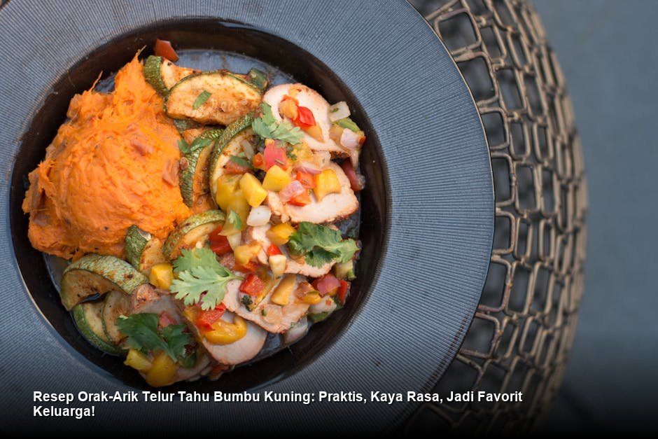 Hidangan orak-arik telur tahu bumbu kuning yang tampak menggiurkan, disajikan di piring putih dengan taburan irisan daun bawang segar di atasnya.