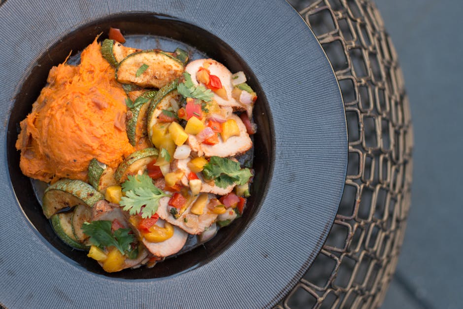 Potongan ayam kecap mentega yang berkilau kecokelatan dengan taburan daun bawang dan irisan bawang bombay segar di atas piring saji putih yang estetik.