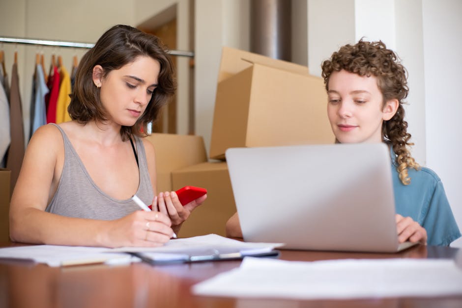 Sepasang profesional muda sedang duduk di sofa, salah satunya memegang laptop sambil tersenyum ke arah pasangannya, menunjukkan momen keseimbangan antara pekerjaan dan waktu bersama.