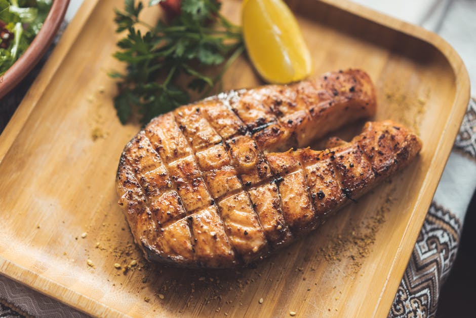 Ayam goreng mentega berwarna cokelat berkilau saus karamel yang menggoda, disajikan estetik dengan taburan daun bawang dan irisan bawang bombay di atas piring putih.