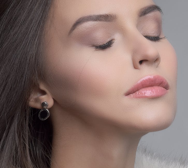 Seorang wanita tersenyum sambil mengaplikasikan pelembap atau tabir surya pada wajahnya sebagai bagian dari rutinitas perawatan kulit pagi hari.